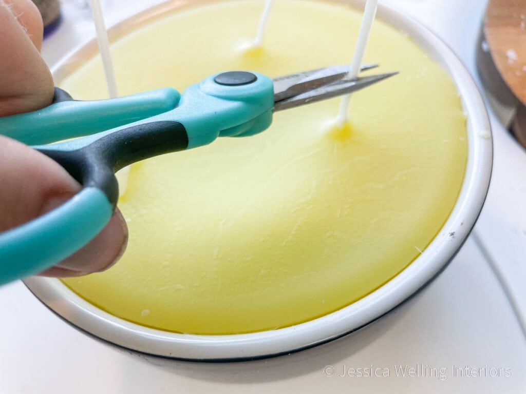 close-up of a hand using scissors to cut the wick of a DIY candle