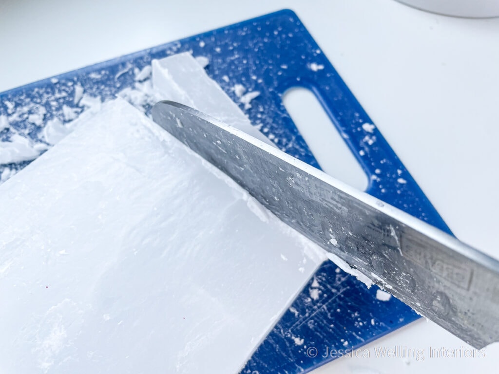 close-up of kitchen knife cutting a large block of paraffin wax into chunks before melting