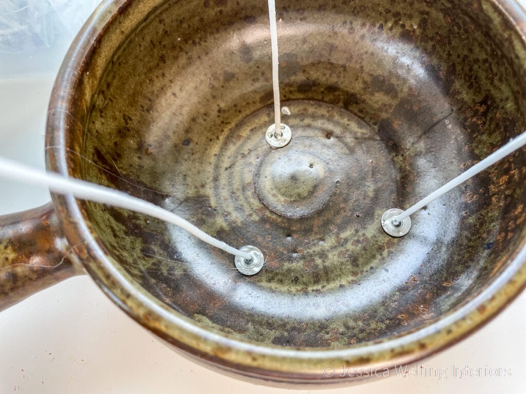 close-up of a rustic bowl with three candle wicks attached to the bottom