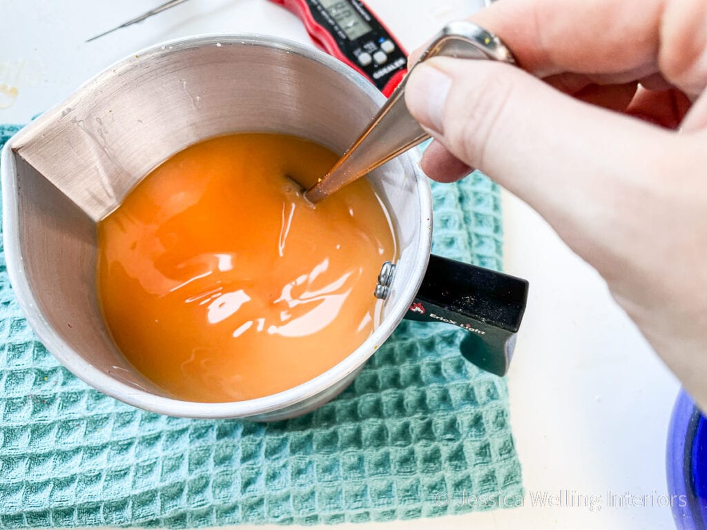 melted paraffin wax being stirred to incorporate the orange wax dye