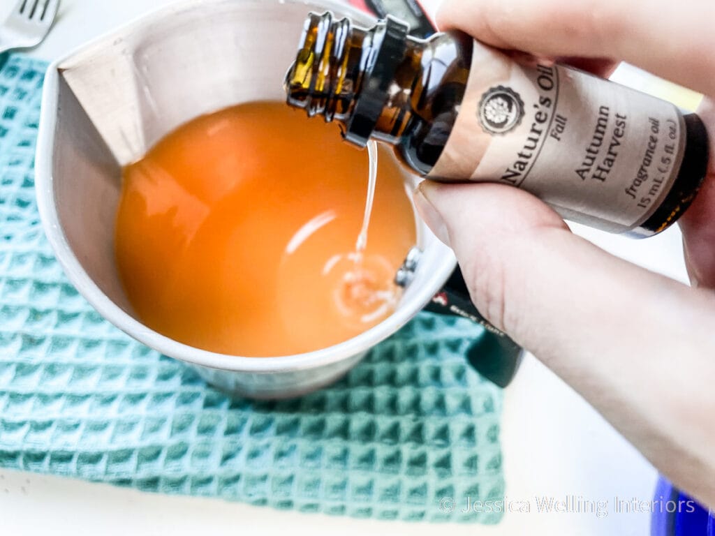 candle fragrance oil being added to metal pitcher of melted orange wax