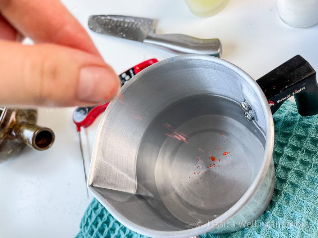 hand sprinkling orange wax dye into a pitcher of melted paraffin wax