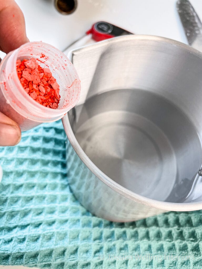 bright orange wax dye chips next to metal pitcher of melted candle wax