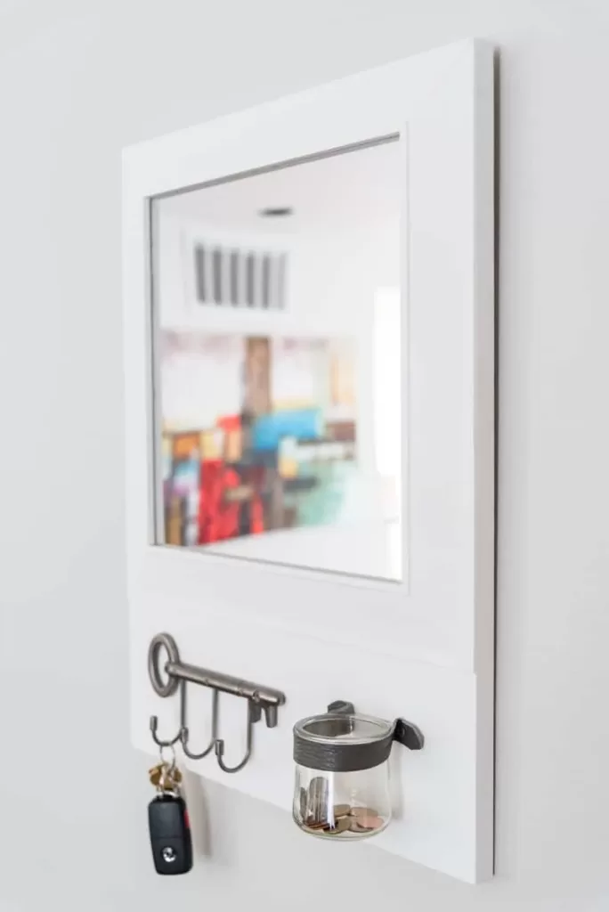 close-up of DIY entryway mirror with hooks for keys, and a change jar