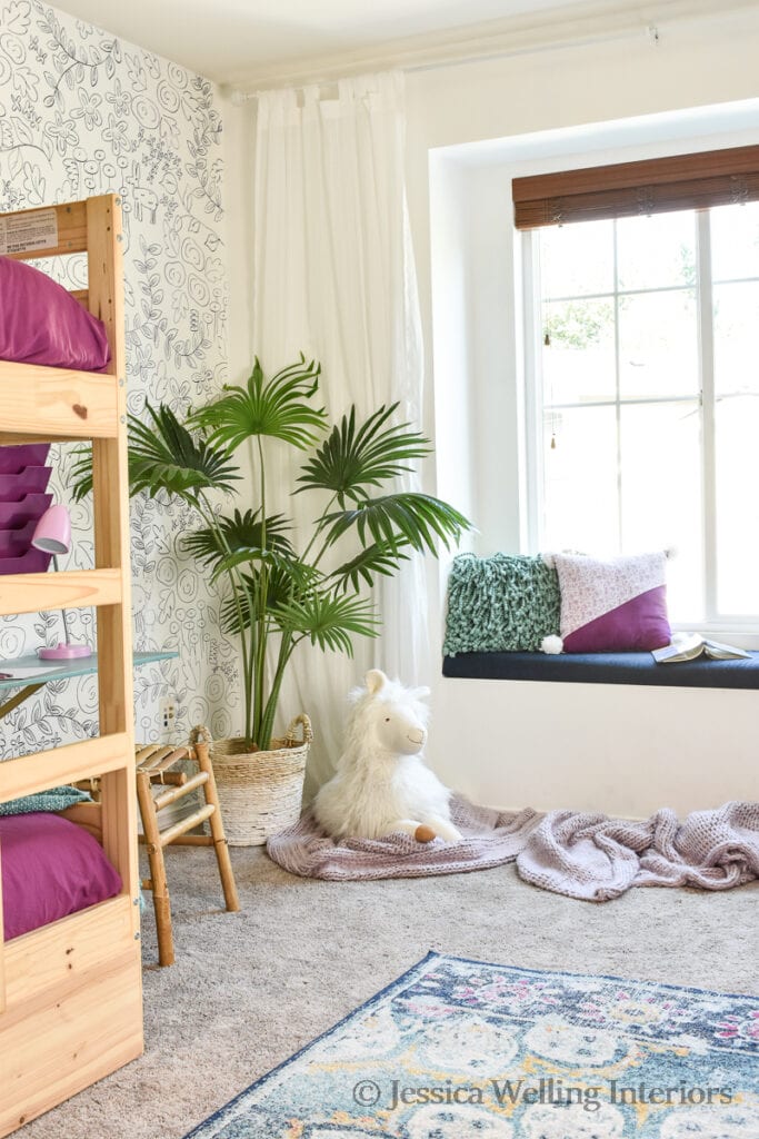 girls' bedroom with Ikea bunk beds, artificial plant, a faux wallpaper accent wall, and a stuffed alpaca