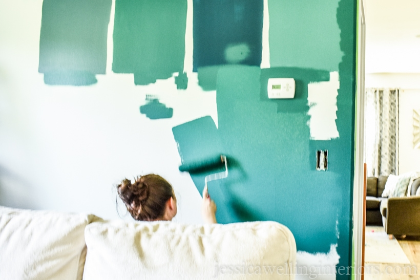 woman painting an accent wall dark green with a paint roller
