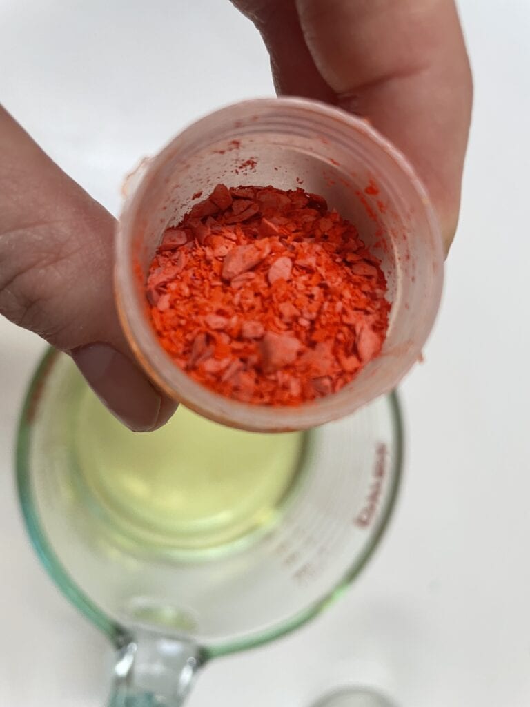 close-up of hand holding a small container of bright orange wax dye chips