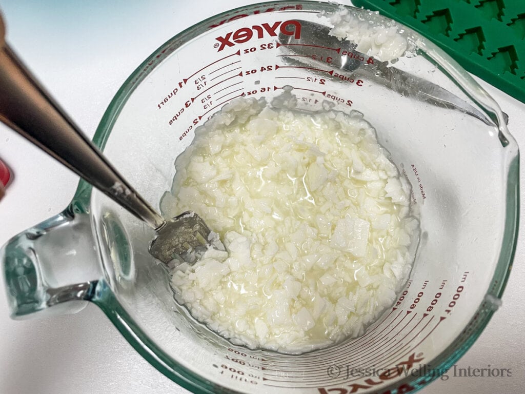 overhead view of glass measuring cup with partially melted soy wax flakes and a fork stirring them