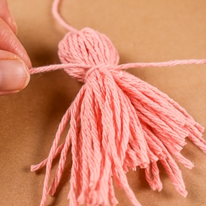 close-up of fingers tying a pink yarn tassel