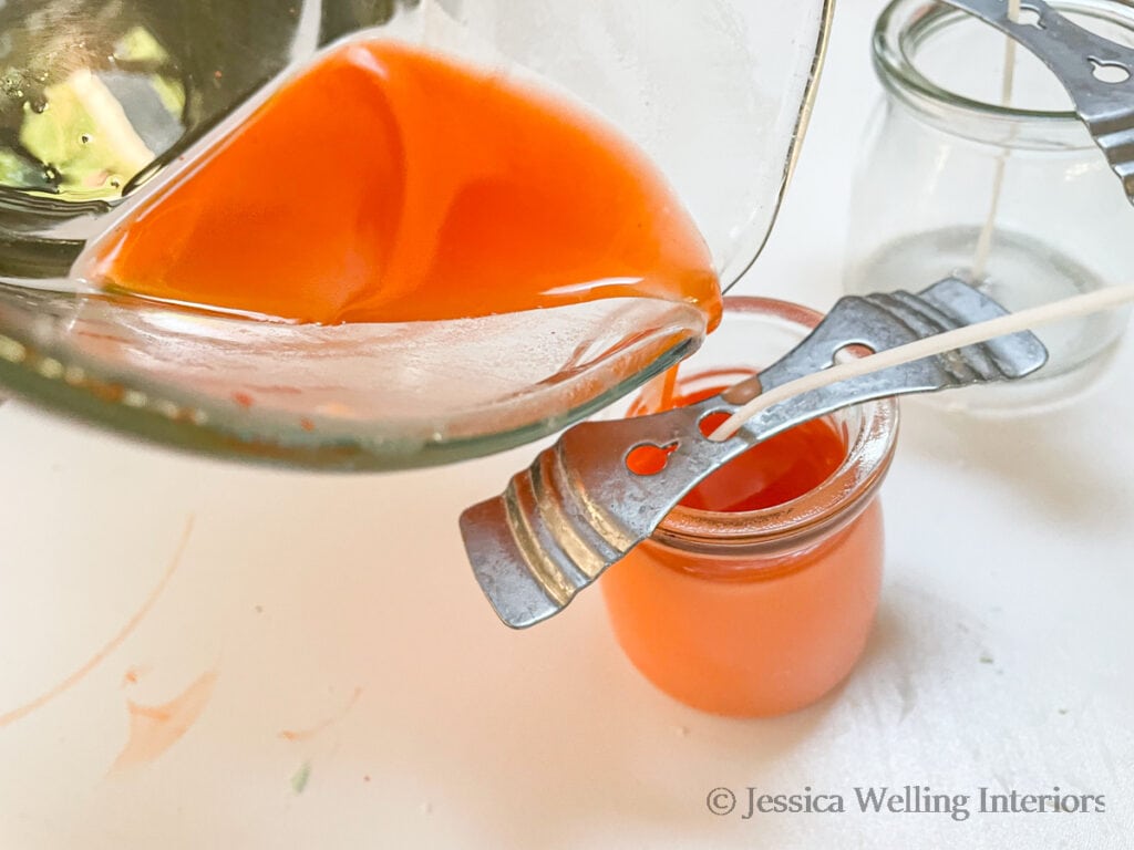 orange candle wax being poured into a glass candle jar