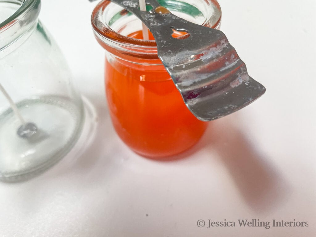 small glass candle jar filled with melted orange wax