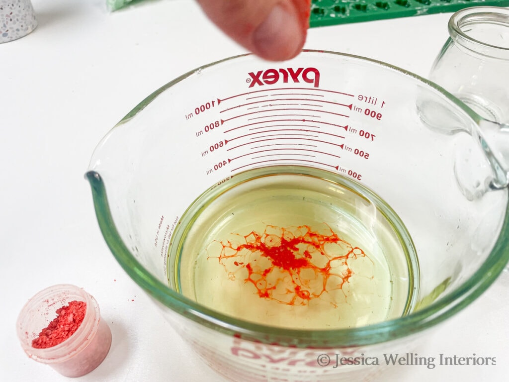 glass measuring cup of melted soy wax with melting orange wax flakes melting on top