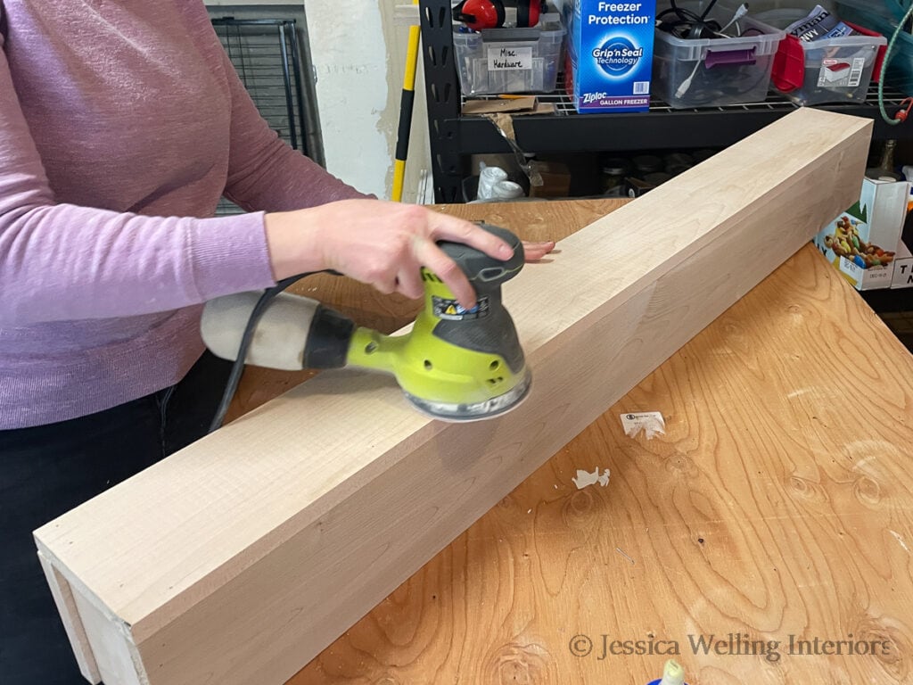 woman using an orbital sander to sand a DIY box beam mantel