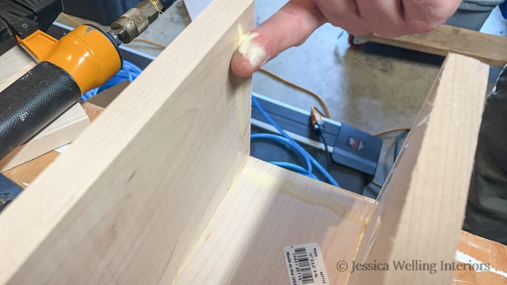 finger applying wood glue to the inside of wood mantel  before attaching the end piece