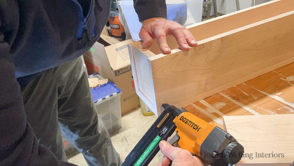 man using a pin nailer to attach pieces of a DIY wood mantel together