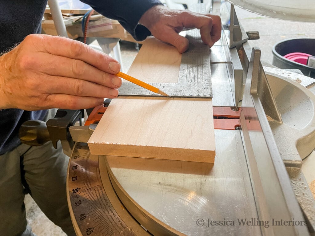 man using a pencil and speed square to mark the end of a board to build a mantel