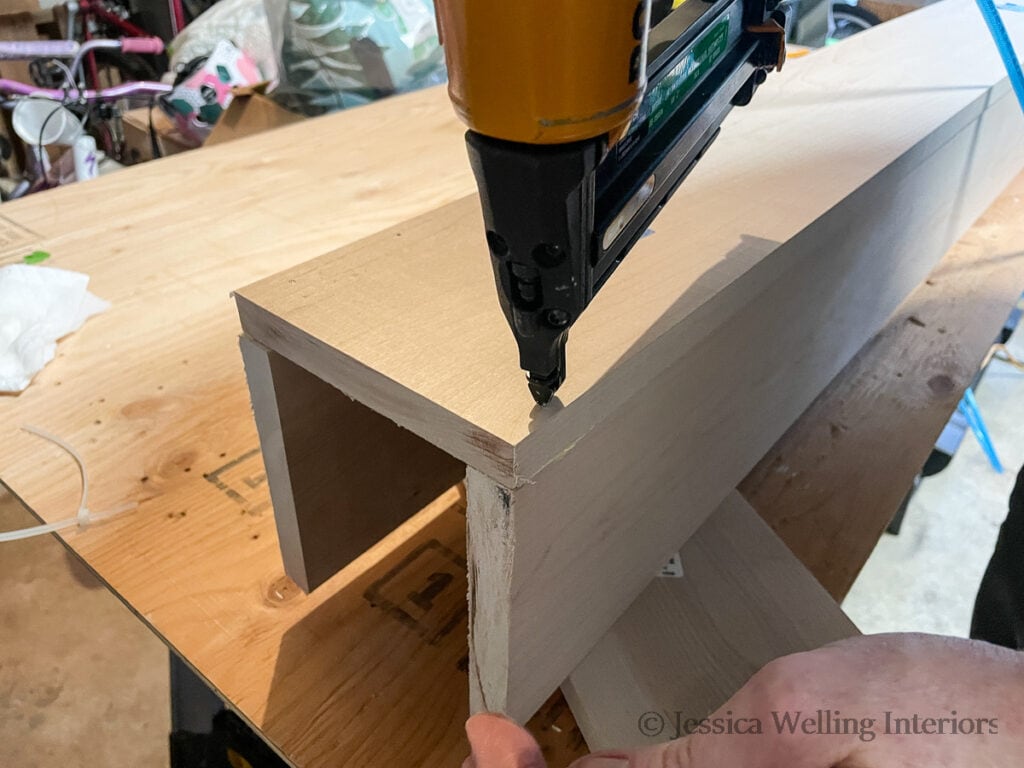 pin nailer attaching the boards together to make a DIY fireplace mantel
