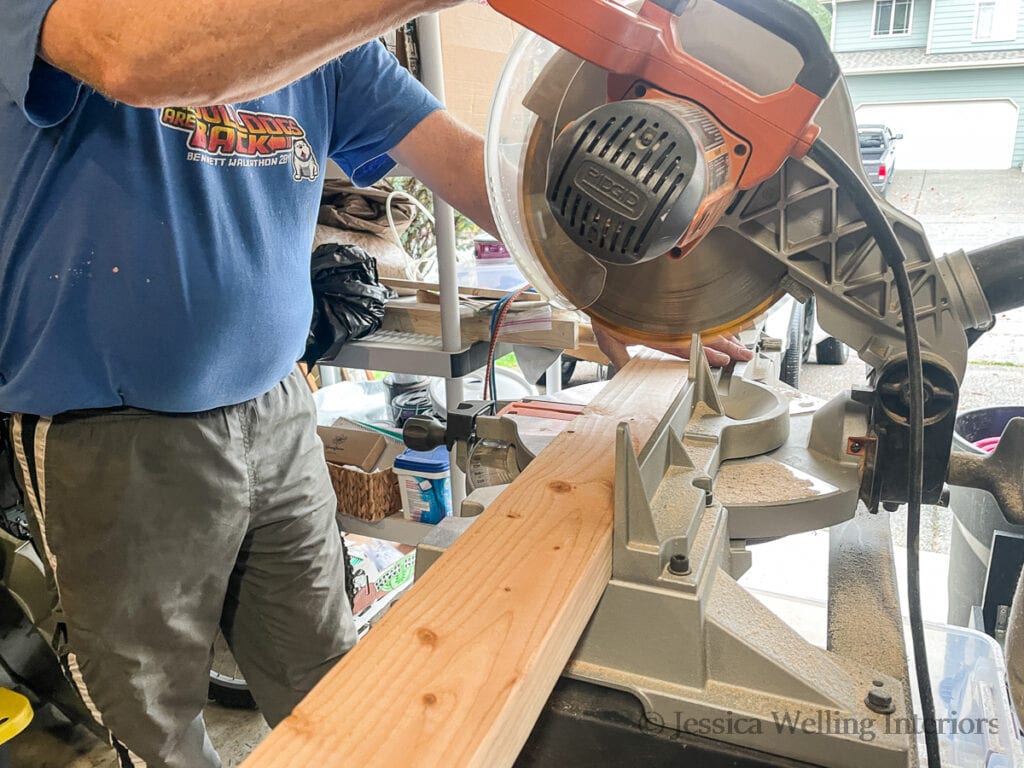 man using a miter saw to cut a 2x4 to mount a DIY fireplace mantel to the wall