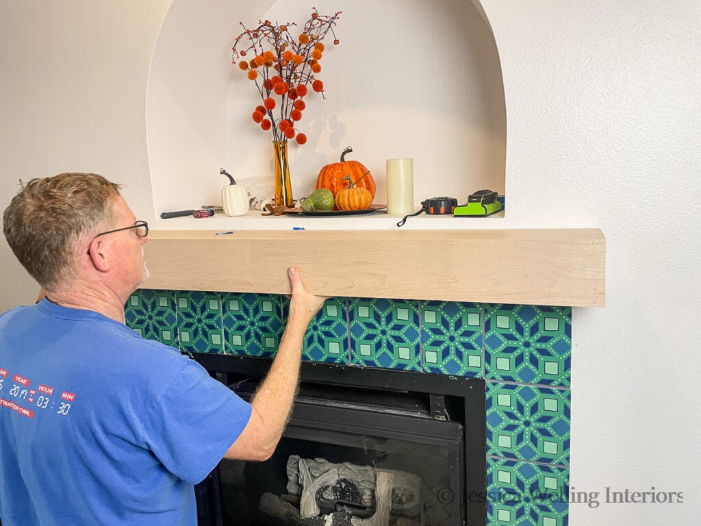 man setting a DIY fireplace mantel in place on the wall above the fireplace