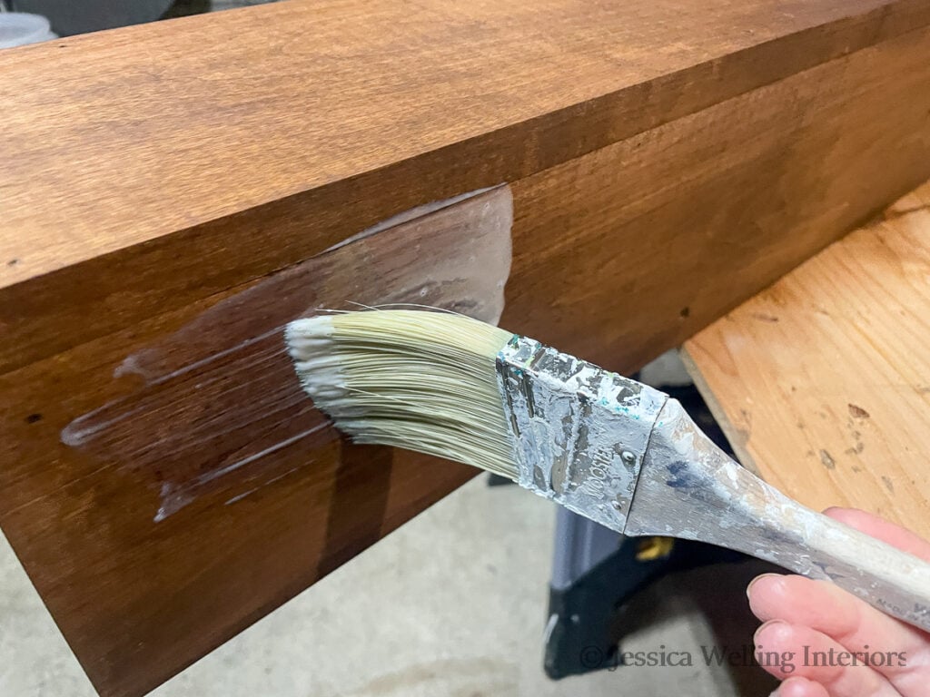close-up of a paintbrush applying polyurethane to a DIY wood mantel
