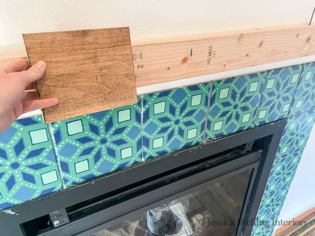 hand holding a wood stain sample up to the fireplace tile