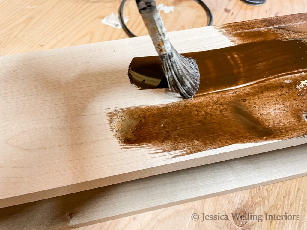 close-up of a paintbrush applying dark brown wood stain to a DIY fireplace mantel