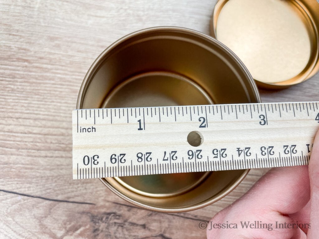 hand using a ruler to measure the inside diameter of a candle tin to determine the best size wick to use with it