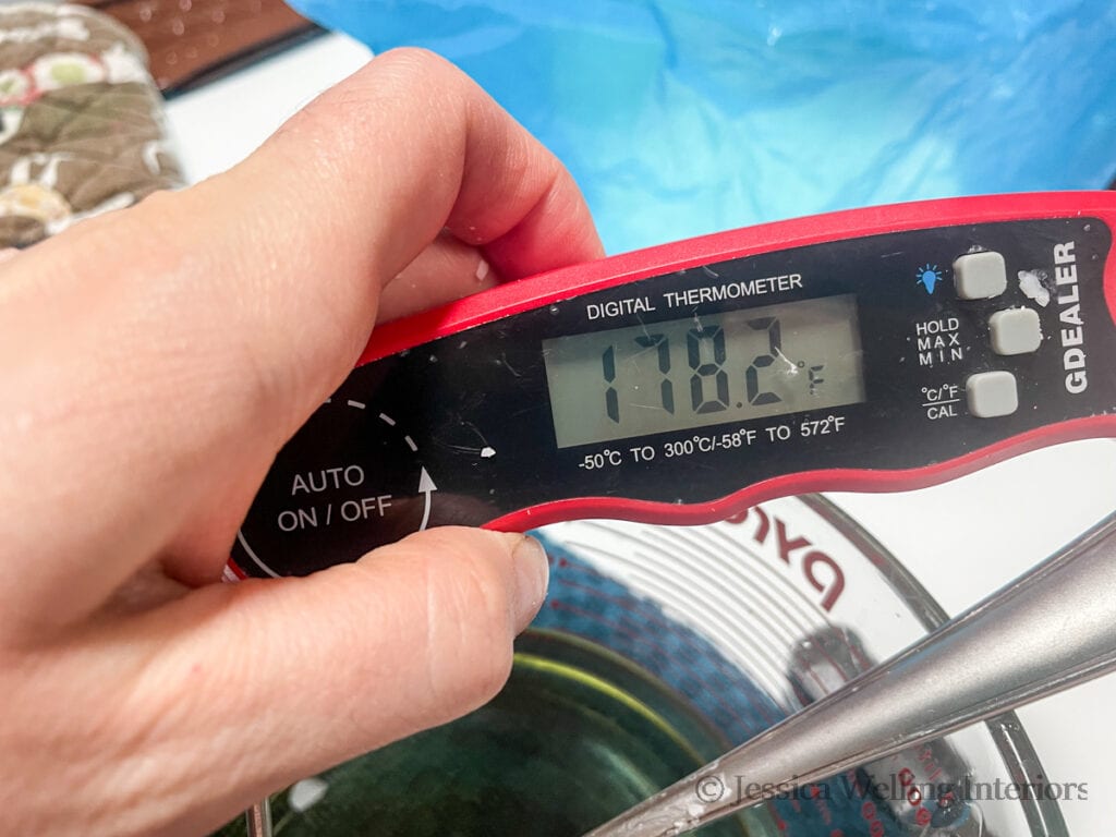 close-up of a hand holding a digital thermometer in a container of hot soy wax