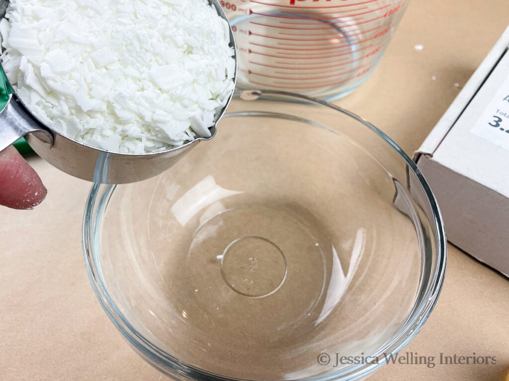 soy wax flakes being measured into a glass mixing bowl to make DIY wax melts
