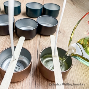 hot candle wax being poured into candle tins with wicks and wick holders in place