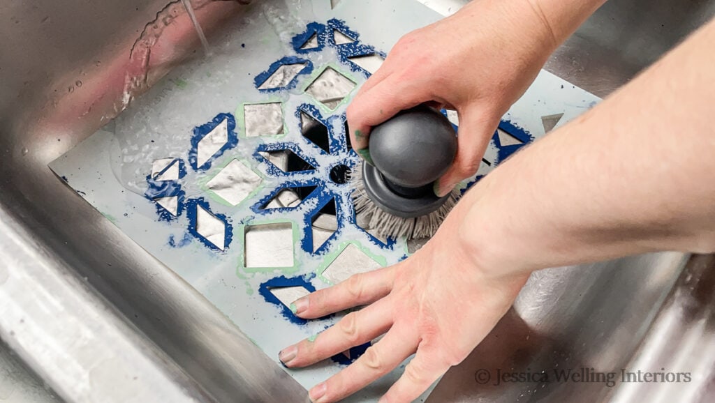hands using a scrub brush to clean a tile stencil in the kitchen sink