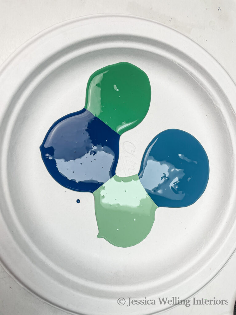 paper plate with four different puddles of paint in greens and blues