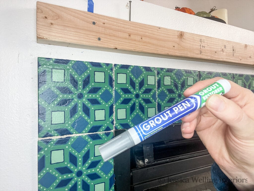 hand holding a dark grey grout pen up in front of tile around fireplace