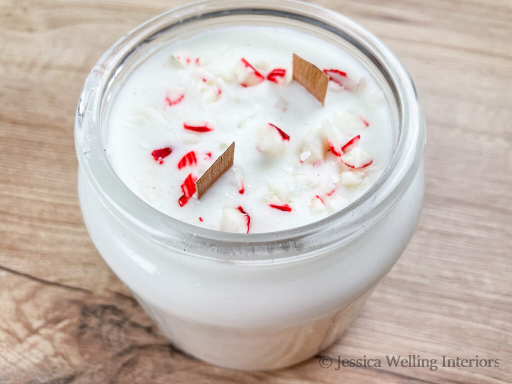 large soy candle in a jar with wood wicks and candycane pieces embedded in it, scented with Peppermint fragrance oil for candles
