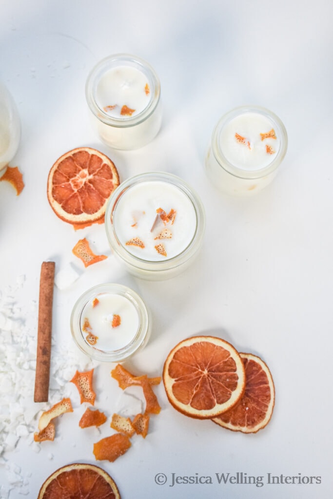overhead view of white soy candles scented with with Candied Citrus Peel fragrance Oil and bits of orange peel, dried orange slices, and cinnamon sticks