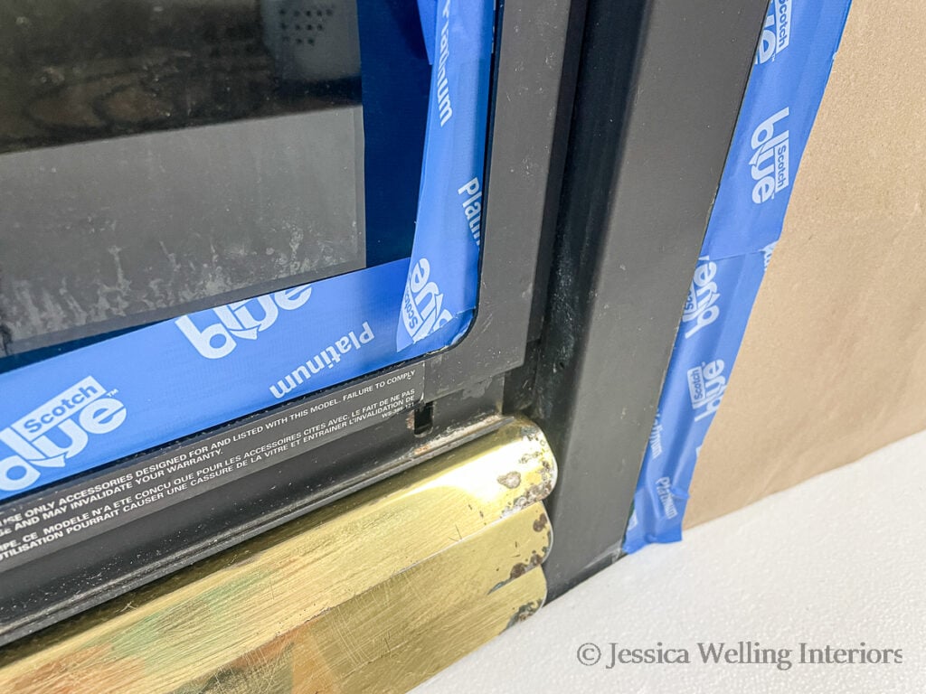 close-up of the bottom of an old gas fireplace insert masked off with masking tape and cardboard before being painted with fireplace spray paint