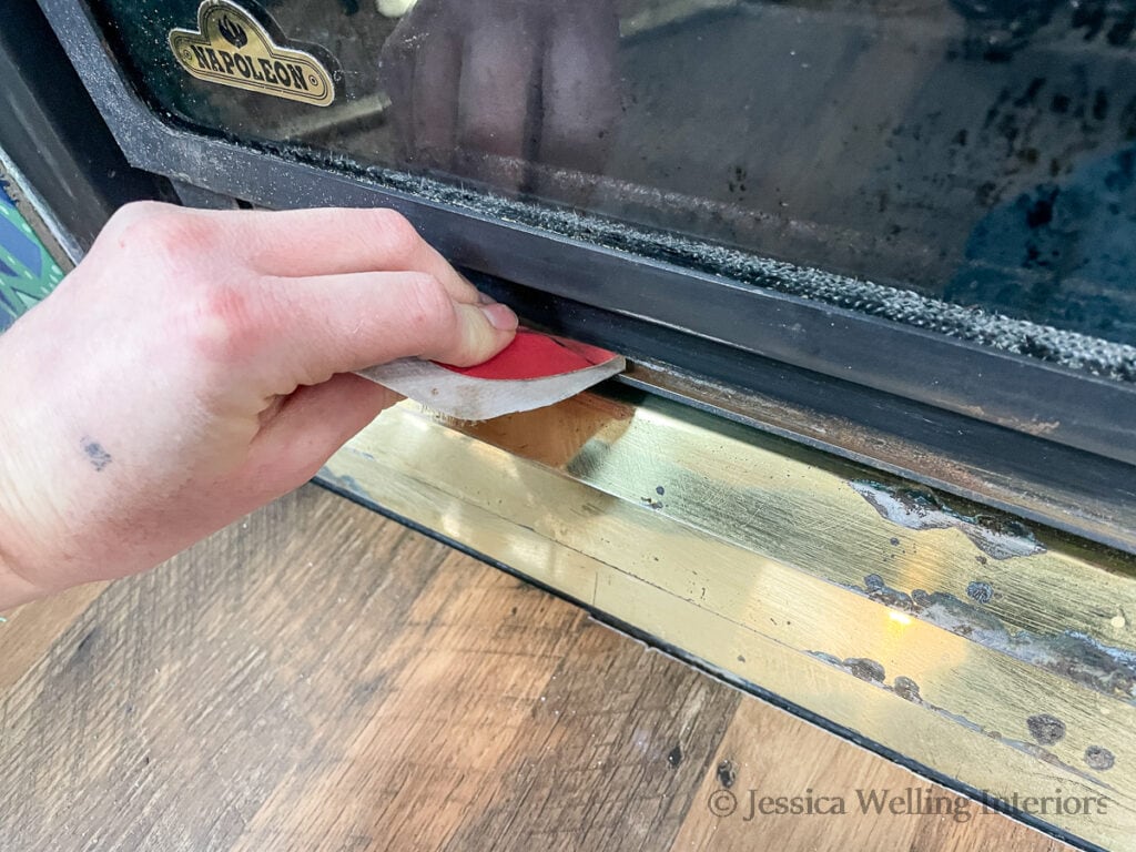 close-up of hand using sandpaper to remove finish from an old fireplace insert before painting it with high heat paint for fireplace