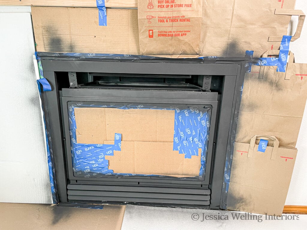 fireplace makeover in progress- fireplace insert masked off with painter's tape and cardboard after being sprayed with the first coat of high heat paint for fireplaces