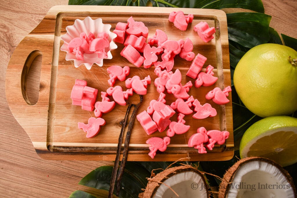 bright pink flamingo-shaped wax melts on a wood cutting board with a coconut and tropical fruit