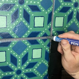 close-up of a hand painting fireplace tile with a grout pen