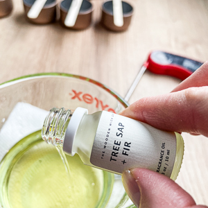 hand pouring candle fragrance oil into a bowl of melted wax