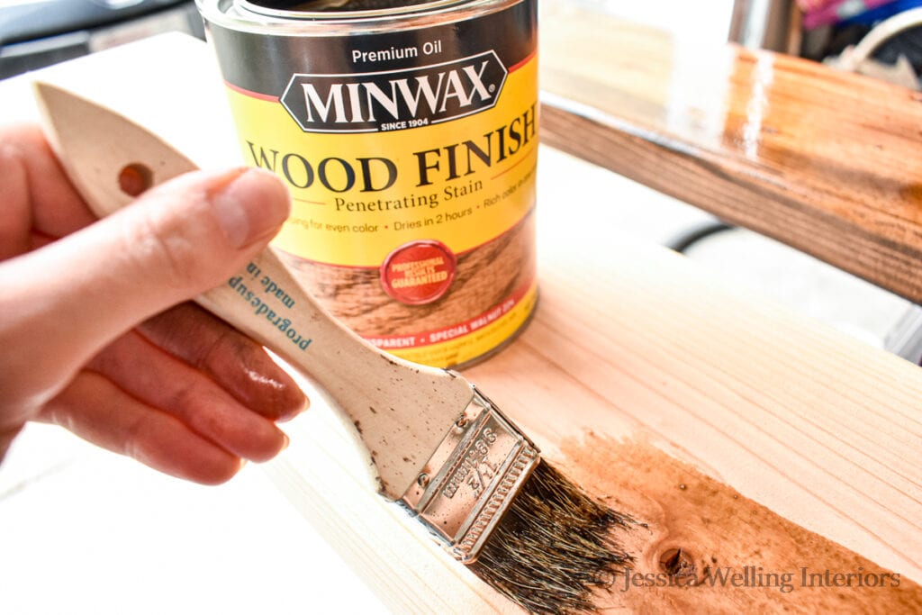 close-up of hand using a chip brush to apply Minwax wood stain to a board