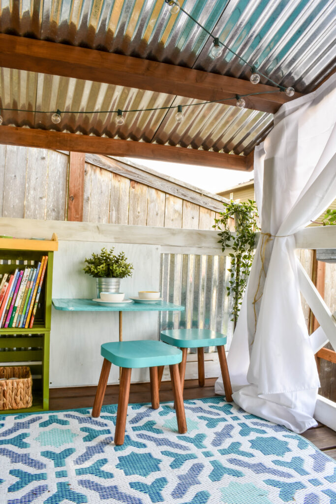 interior of children's playhouse with a small table and stools and a woven plastic outdoor rug in turquoise