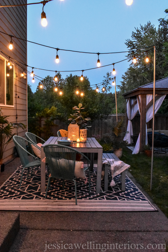 patio dining space with a table & chairs, outdoor rug, and glowing string lights