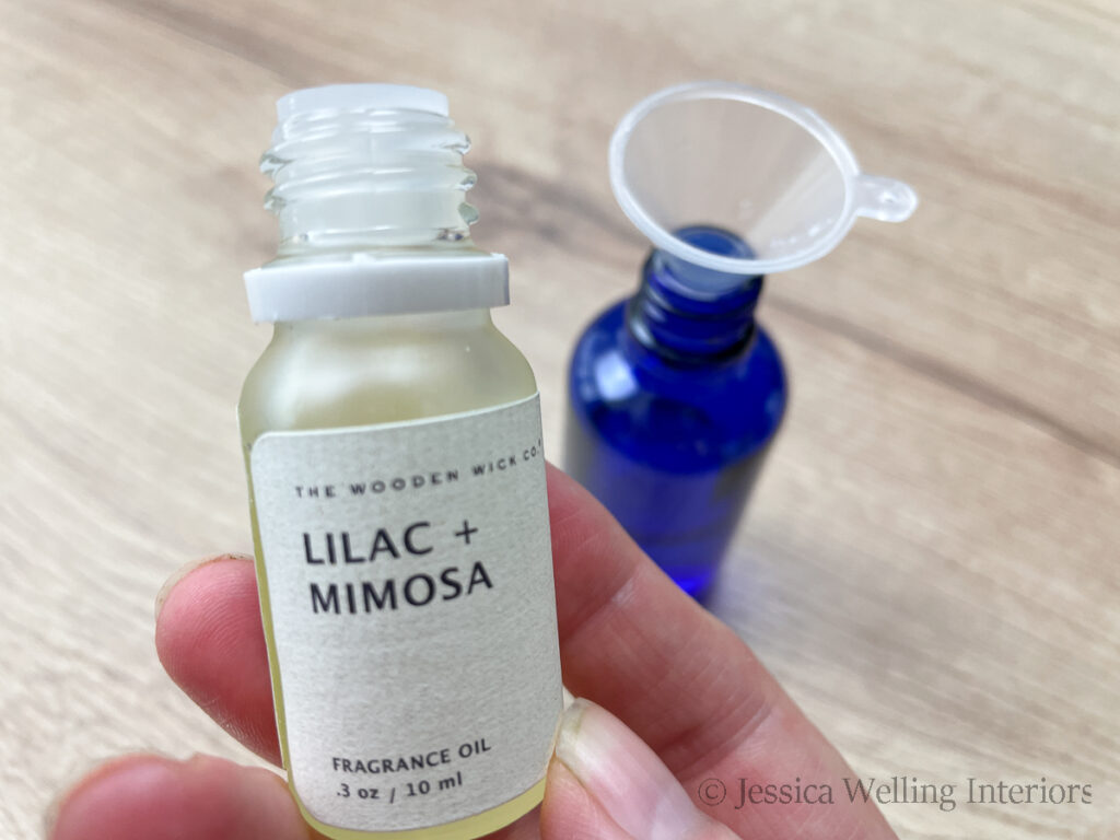 close-up of a bottle of lilac & mimosa fragrance oil  with a blue glass spray bottle of DIY room spray in the background