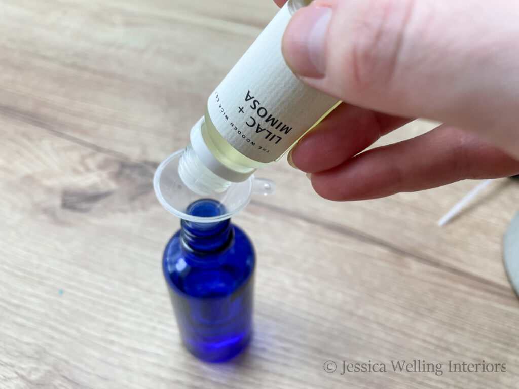 hand pouring lilac & mimosa fragrance oil into a glass bottle using a small plastic funnel