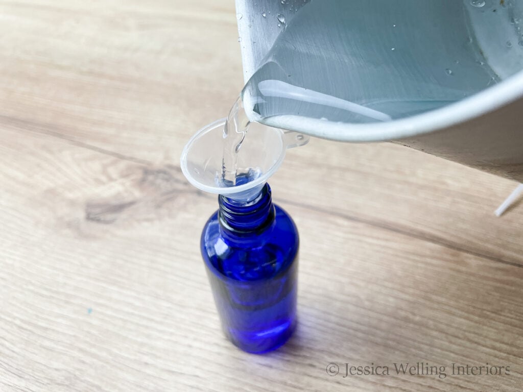 distilled water being poured from a pitcher into a small glass bottle to make DIY room spray