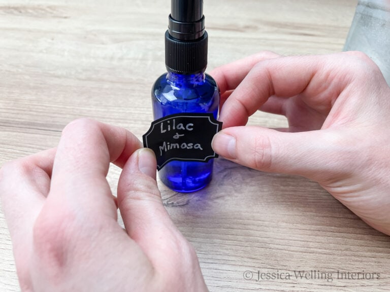 hands putting a sticker label onto a blue glass bottle of DIY room spray