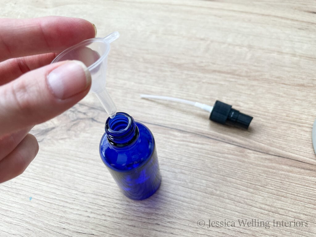 overhead view of hand placing a small plastic funnel into the mouth of a glass spray bottle