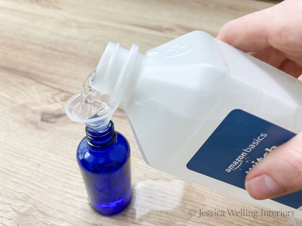 hand pouring witch hazel into a small blue glass bottle to make natural room spray